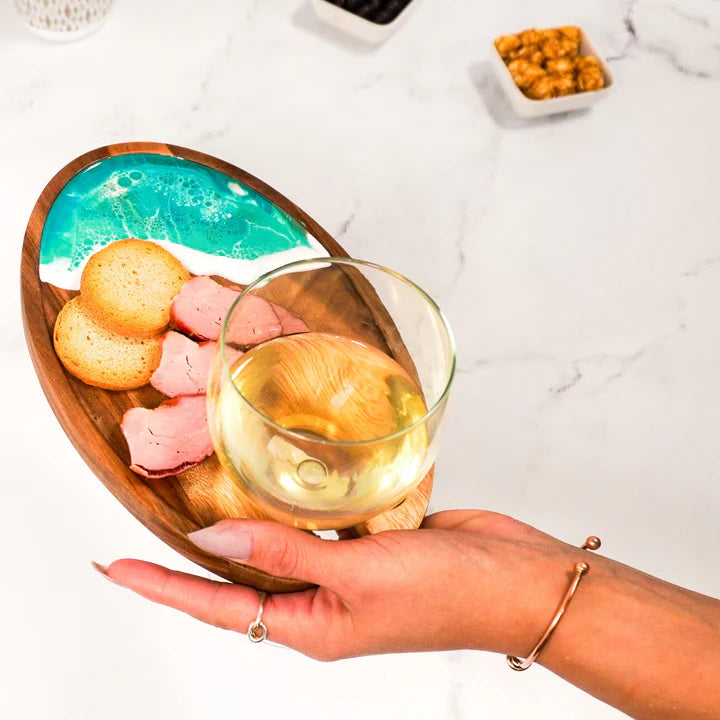 Wooden platter with snacks and a glass of white wine held by a hand on a light background