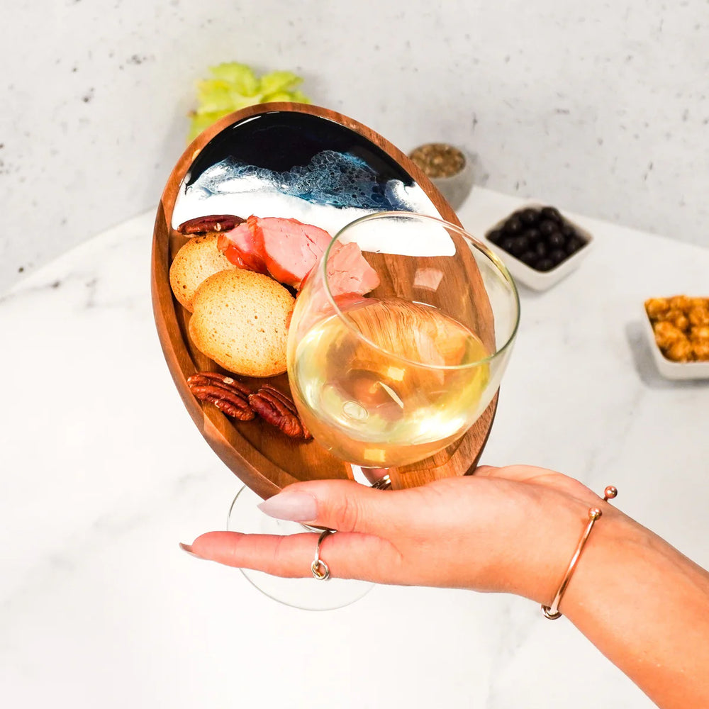 Hand holding a glass of white wine with a charcuterie board in the background