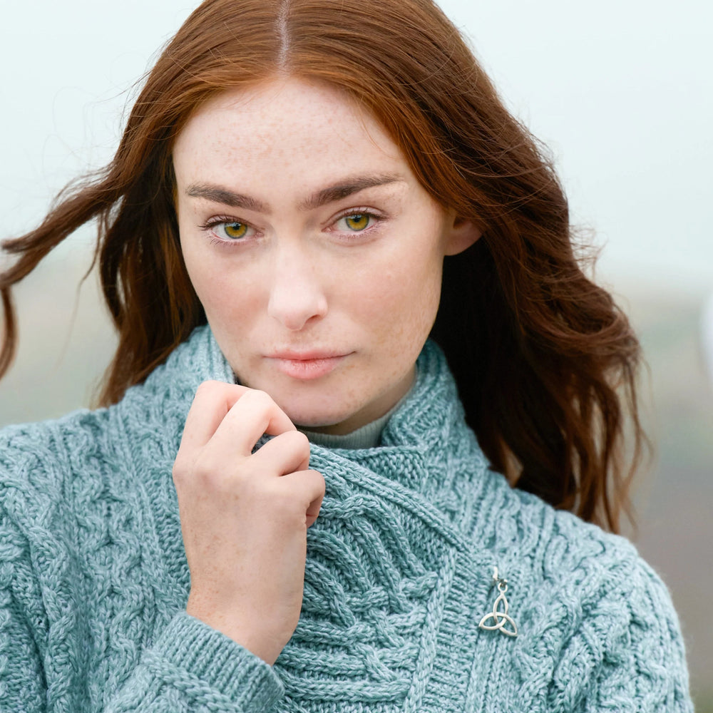 Woman wearing a teal cable knit sweater with a brooch against a light background