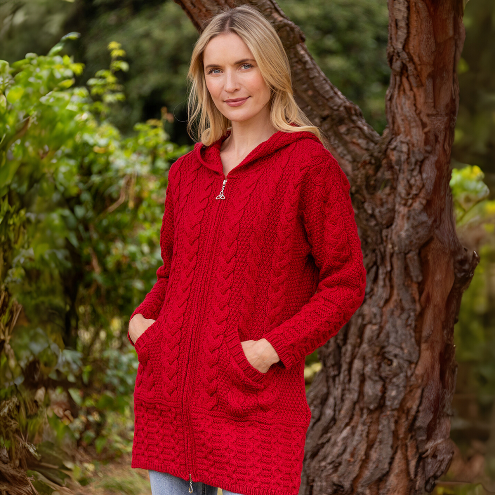 Woman wearing a red knitted hoodie standing next to a tree in a forest setting