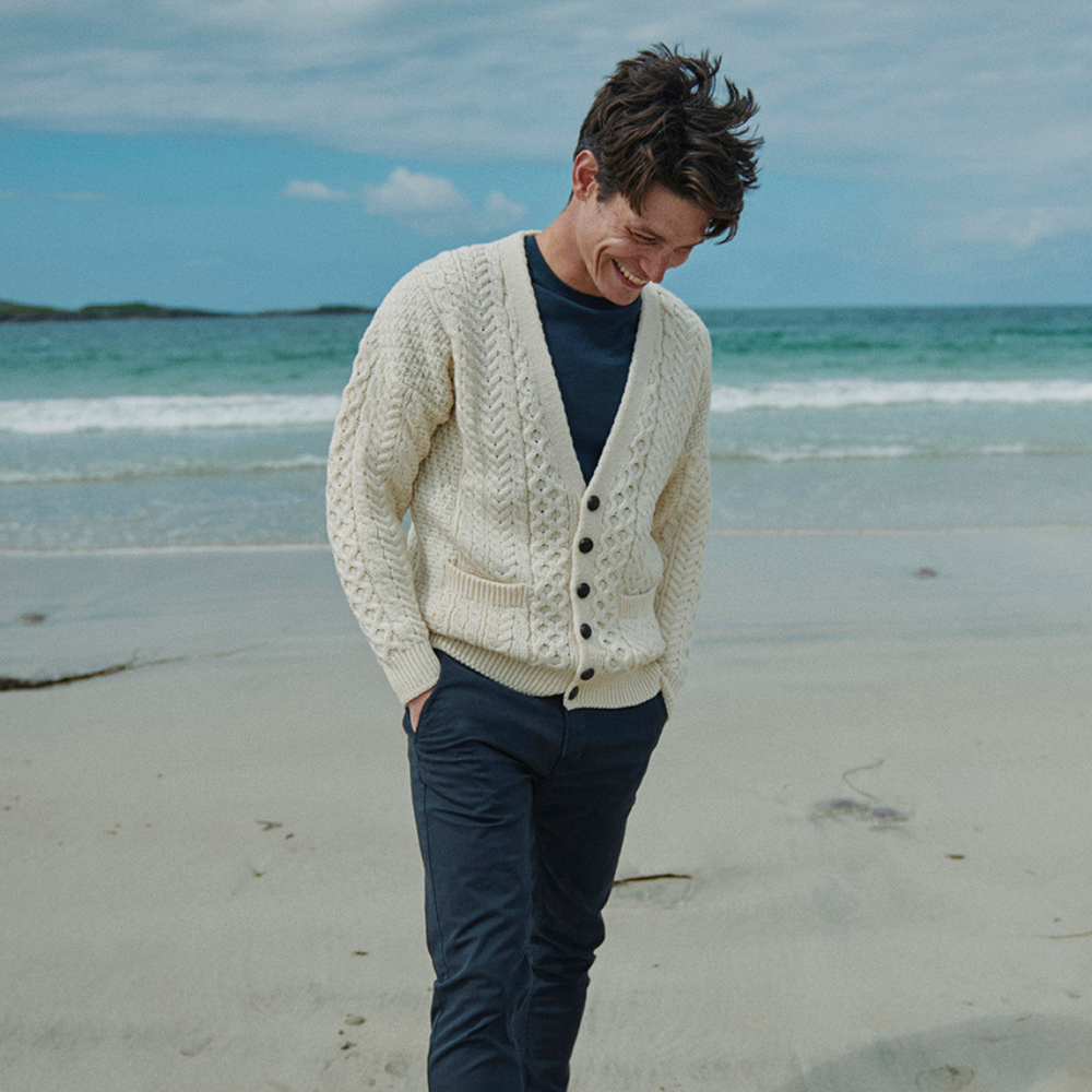 Man wearing a cream cardigan on a beach with ocean in the background