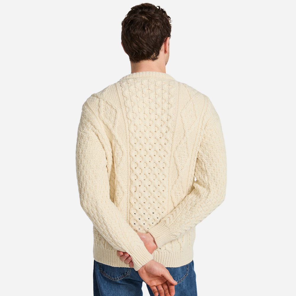 Man wearing a cream cable knit sweater on a plain background