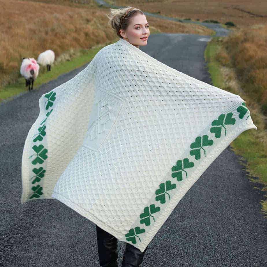 Woman wearing a large white knitted shawl with green patterns on a rural road.