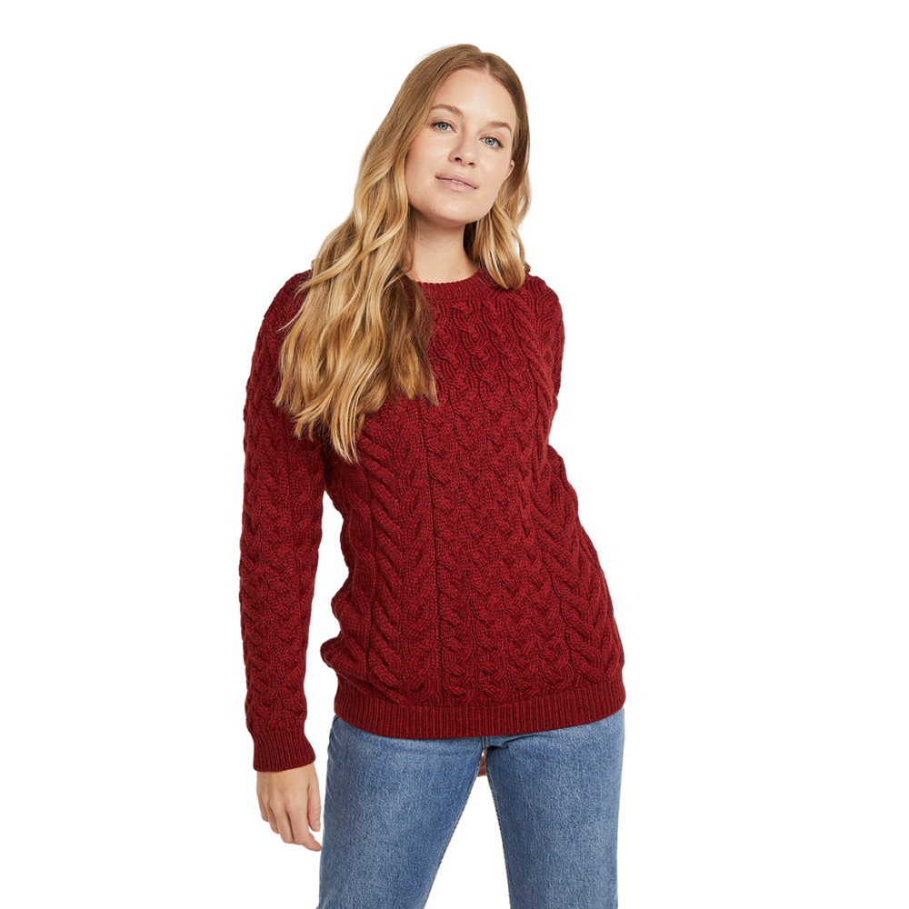 A woman wearing a red crew neck sweater with a classic Aran cable pattern, paired with blue jeans.
