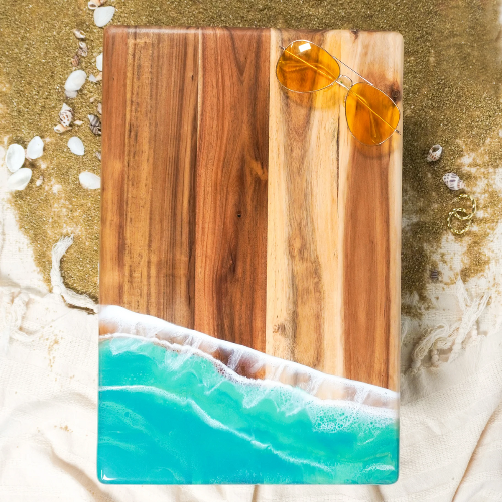 An acacia wood bread board with a caribbean blue epoxy resin representing an ocean wave design.