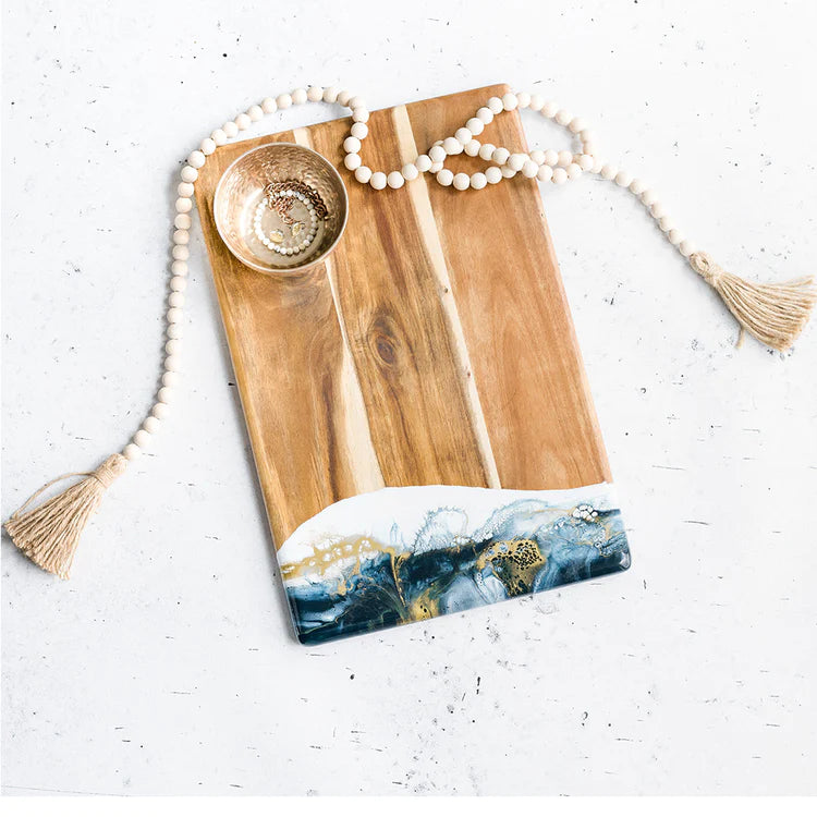 An acacia wood bread board with a blue and gold resin accent, part of the Lynn & Liana Sapphire Sky collection.