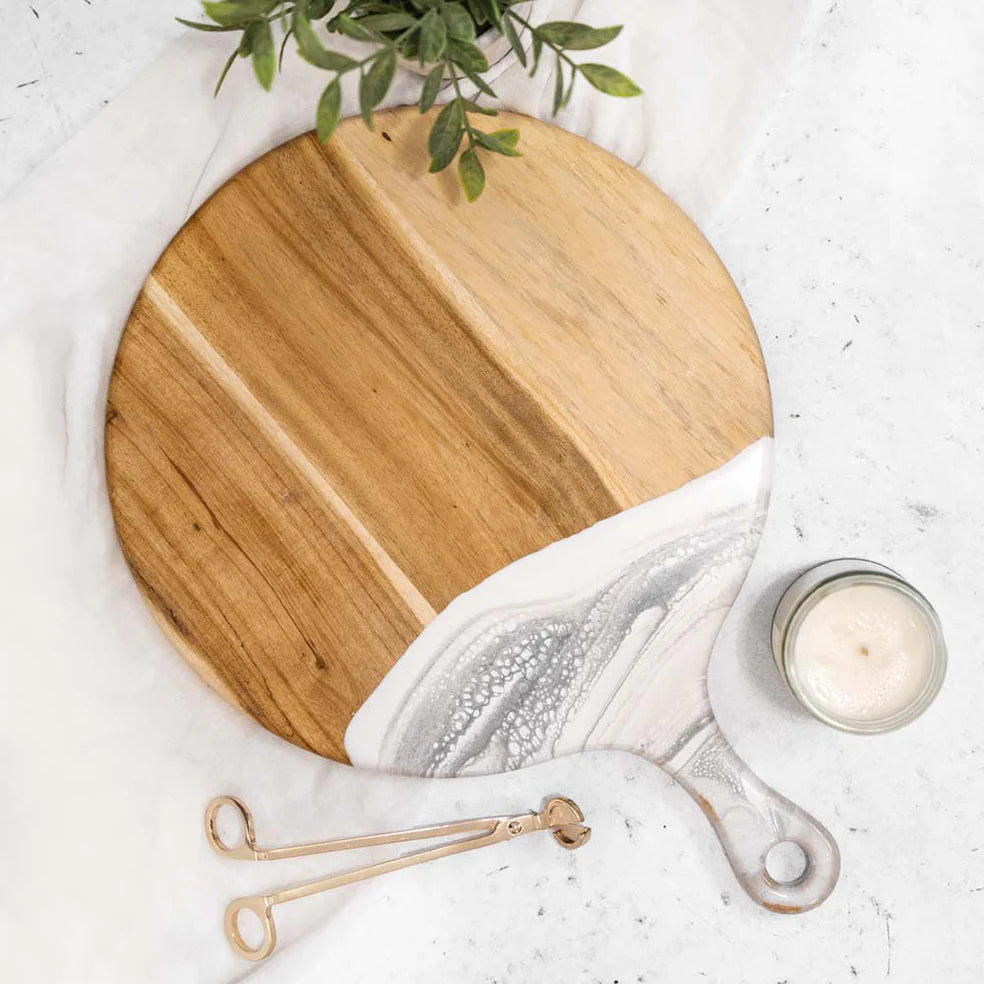 A round cheese paddle with a wooden appearance and a white marble-like pattern towards the edge, with a visible handle.