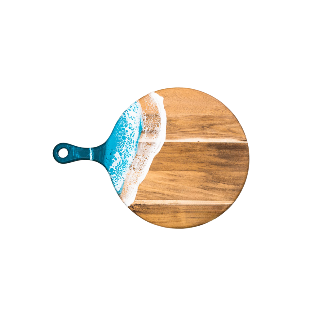 A round cheese paddle with a wooden appearance and a OCEAN WAVES pattern towards the edge, with a visible handle.