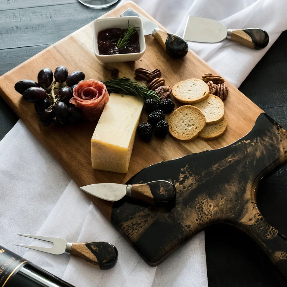 A set of four cheese knives with wooden handles and stainless steel blades, displayed on serving board.