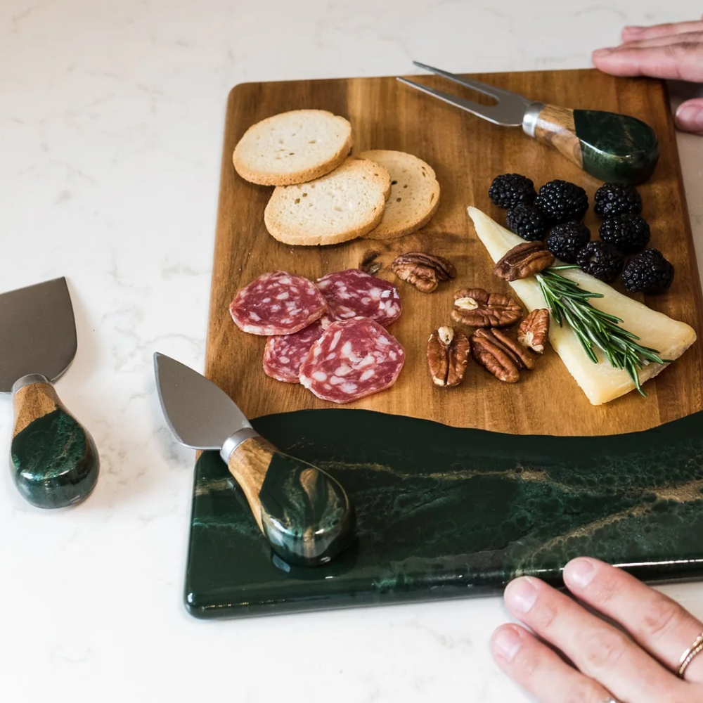 A set of four cheese knives with wooden handles and stainless steel blades, displayed on serving board.