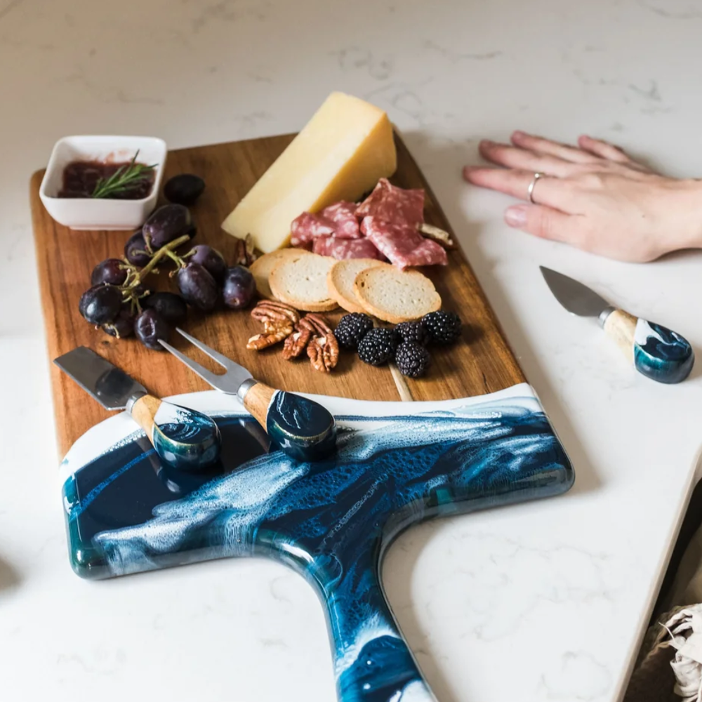 A set of four cheese knives with wooden handles and stainless steel blades, displayed on serving board.