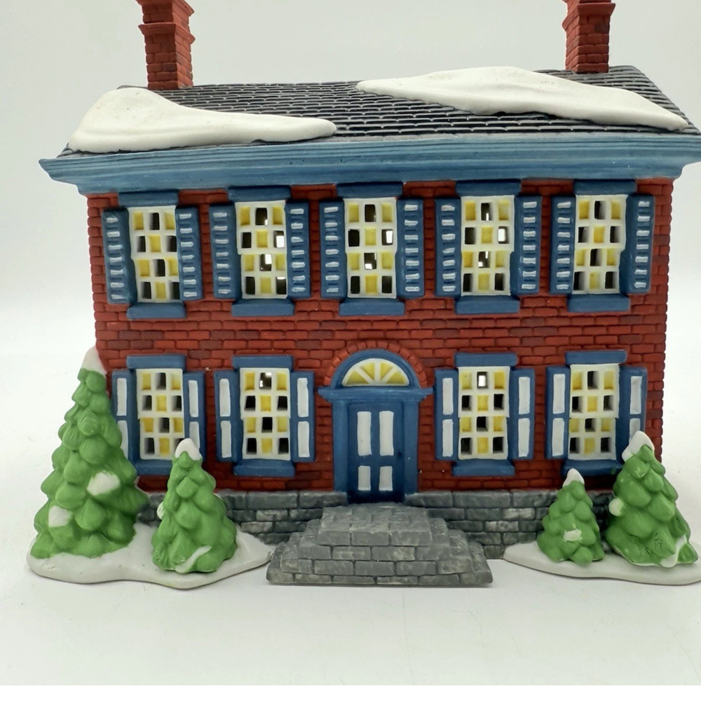 Decorative model of a two-story house with green trees in front on a white background