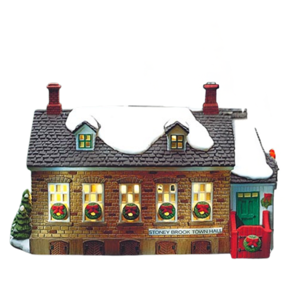 Decorative model of a town hall building with lit windows and snow on the roof, featuring Christmas wreaths.