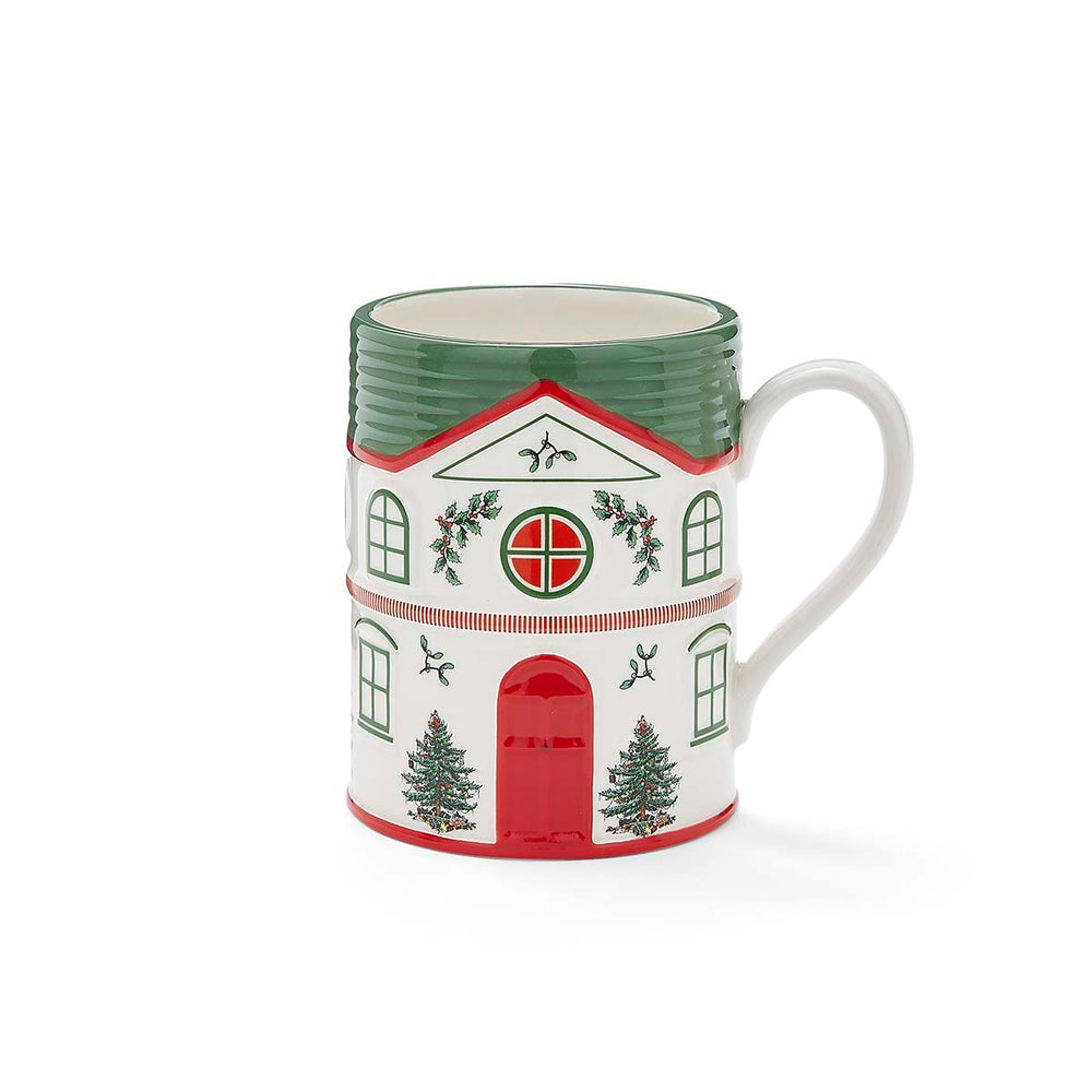 Festive mug shaped like a house with a green roof and handle. Decorated with red doors, windows, Christmas trees, and holly, conveying a seasonal vibe.