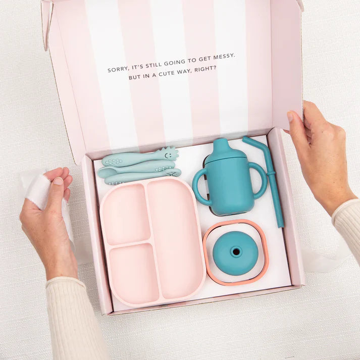Baby utensils set in a pink box with text, held by a person.