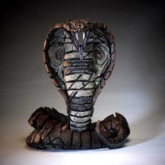 A sculpture of a cobra snake with a copper brown color, displaying detailed textures and a striking, defensive posture.