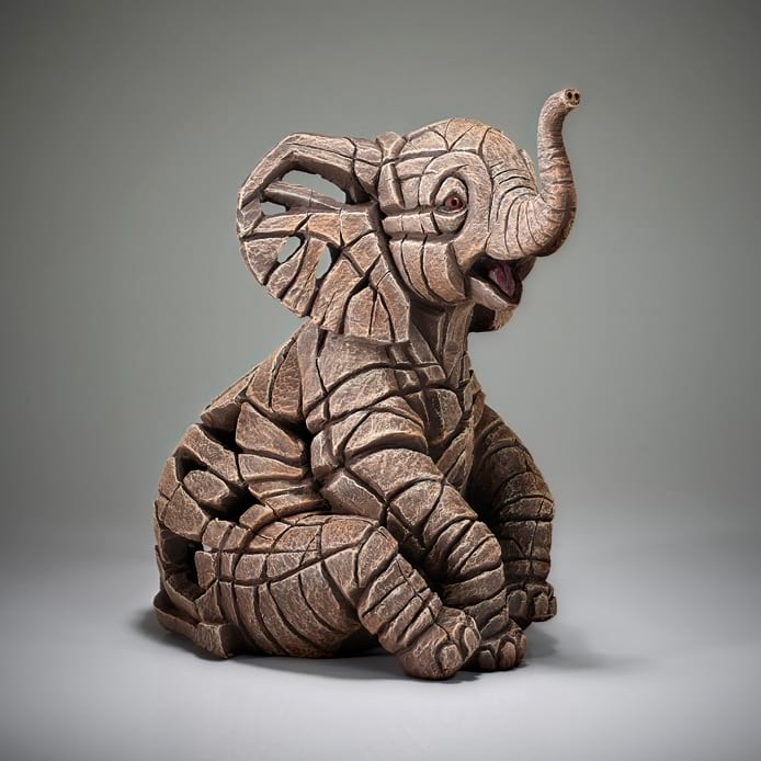 A sculpture of a baby elephant calf, with a textured and rugged finish, displayed against a neutral background.