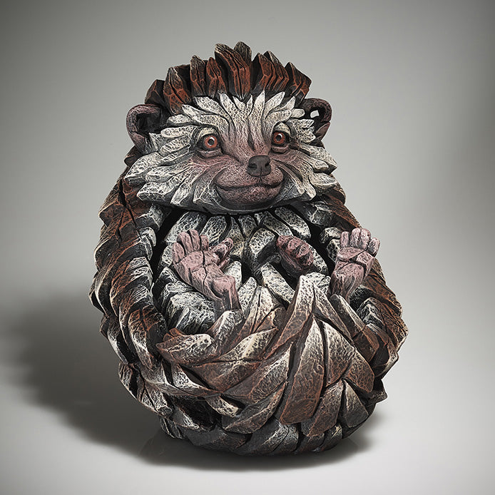 A sculpture of a hedgehog with a combination of brown, beige, and gray colors, featuring a smiling face and detailed quills.