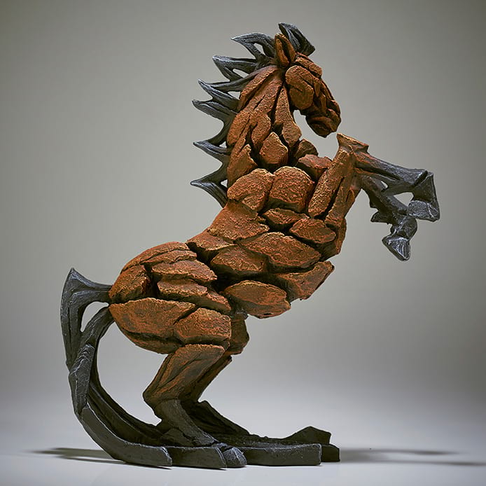 A sculpture of a bay horse in a dynamic standing pose with textured details, primarily in brown tones with black accents.