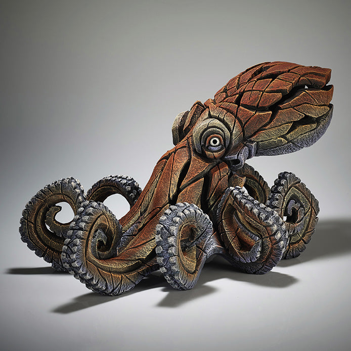 A sculpture of an octopus with a brownish-gray tentacle-like texture and a human eye detail on the top, set against a gray background.