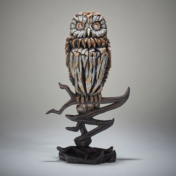 A detailed sculpture of an owl perched on a branch, with a predominantly brown and white color palette.