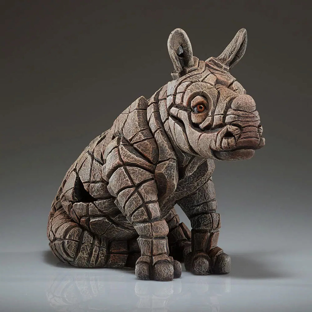 A sculpture of a rhinoceros calf with a textured, rugged appearance, predominantly in brown tones.
