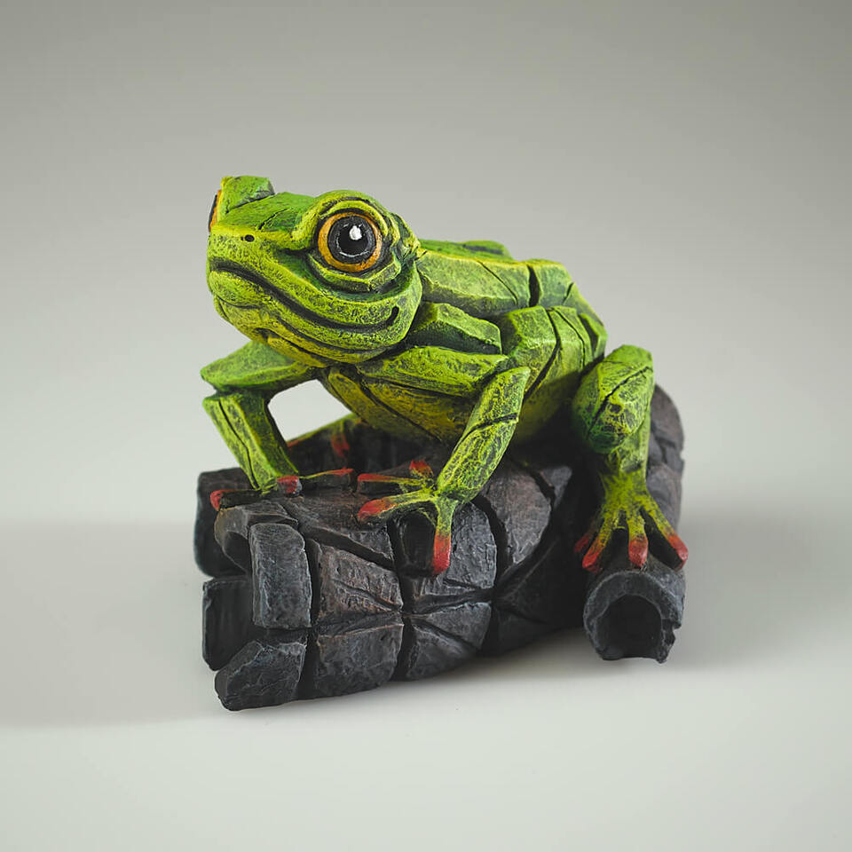 A green frog sculpture with red details on its toes, perched on a dark, textured surface.