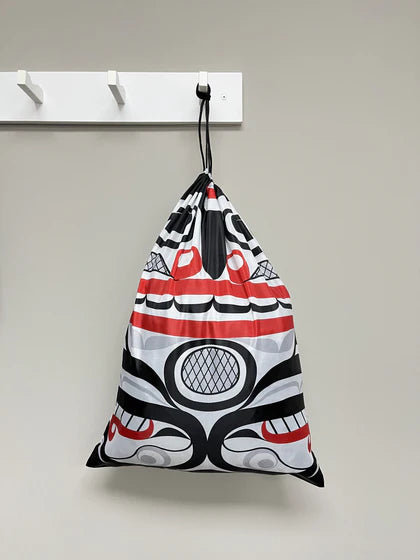 Drawstring bag with a red, black, and white pattern hanging on a white rack against a beige wall.