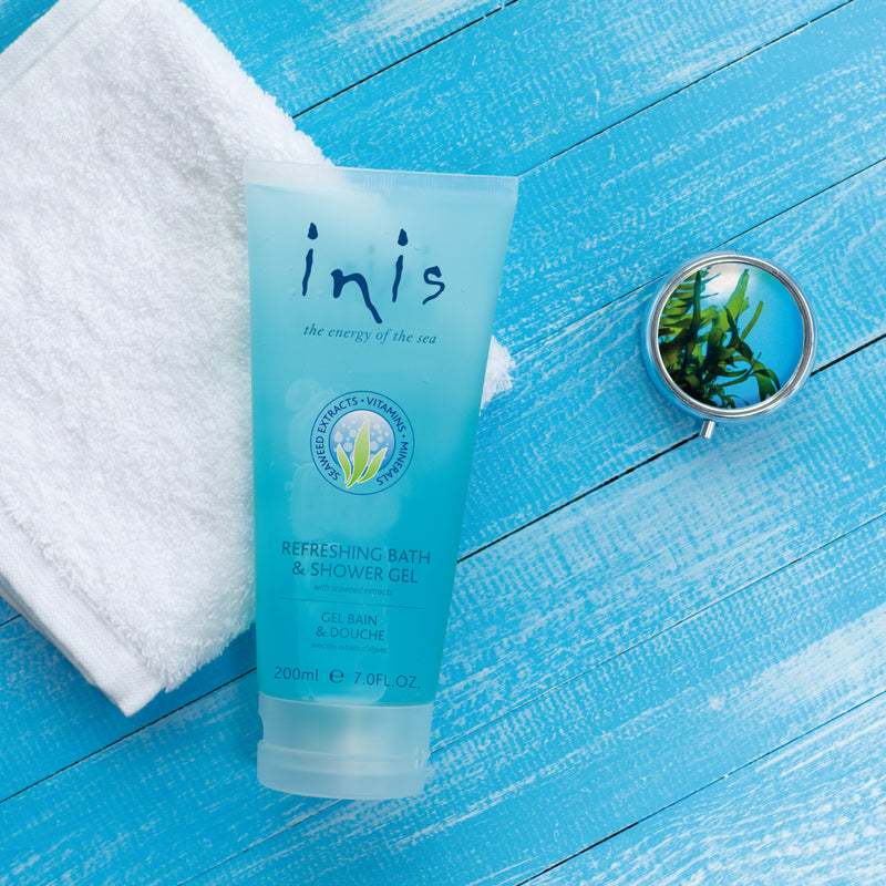 Blue tube of 'inis' bath and shower gel on a blue wooden surface with a towel and mirror.