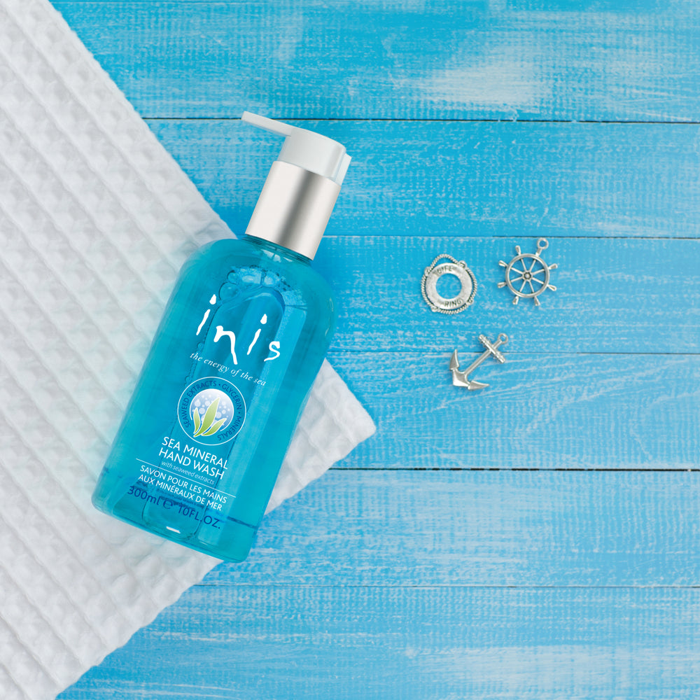 Blue bottle of inis Sea Mineral Hand Wash on a blue wooden surface with decorative items.