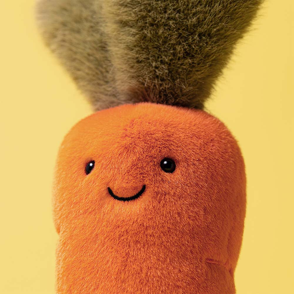 Plush toy carrot with a smiling face on a yellow background