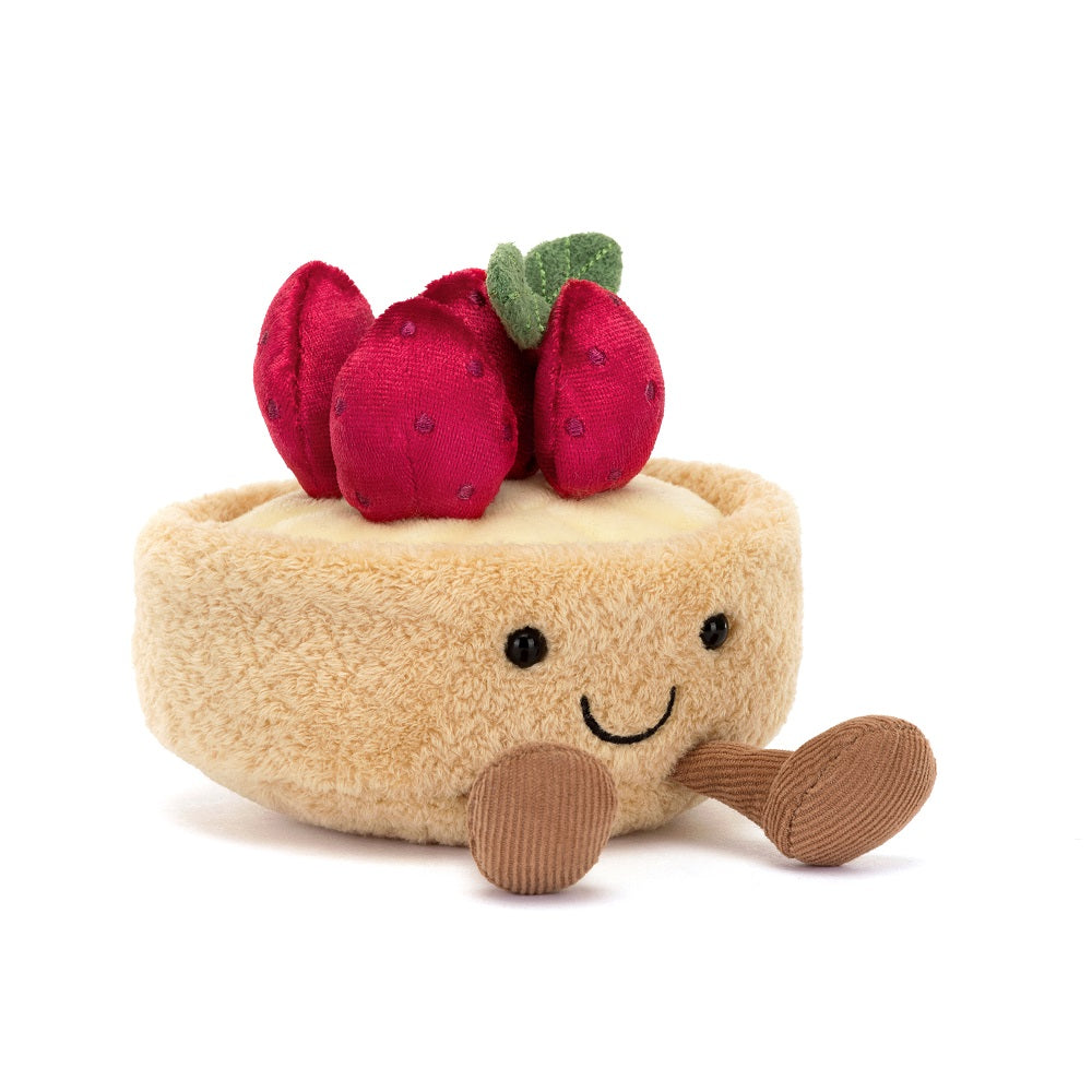 A plush toy resembling a tarte aux fraises with a golden brown color, strawberries, and green leaves embroidered on it. It has a smiling face with stitched details.