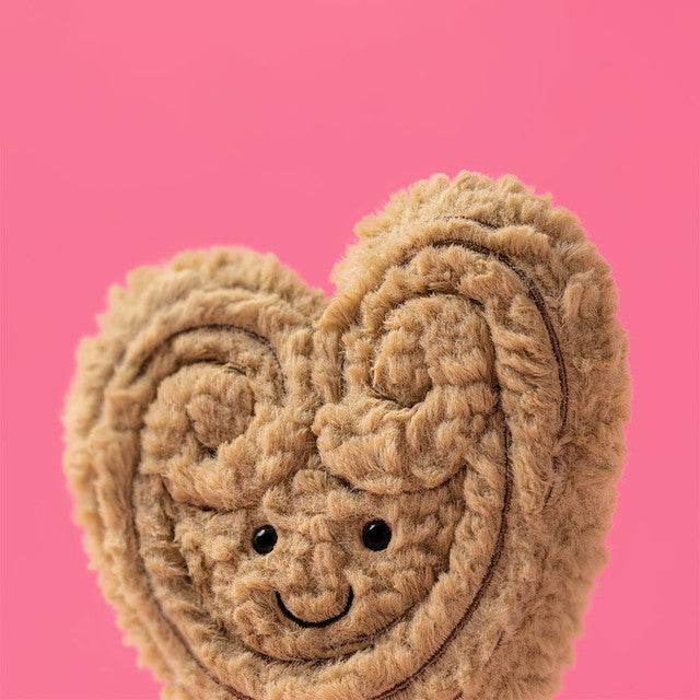 Heart-shaped plush toy with a smiling face on a pink background