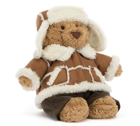 A plush teddy bear wearing a brown and cream winter parka with ear flaps and brown corduroy pants, photographed on a clean white background.