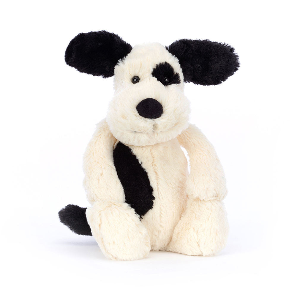 A silky-soft black and cream colored plush puppy toy with a smudgy black patch and sooty tail, sitting upright.