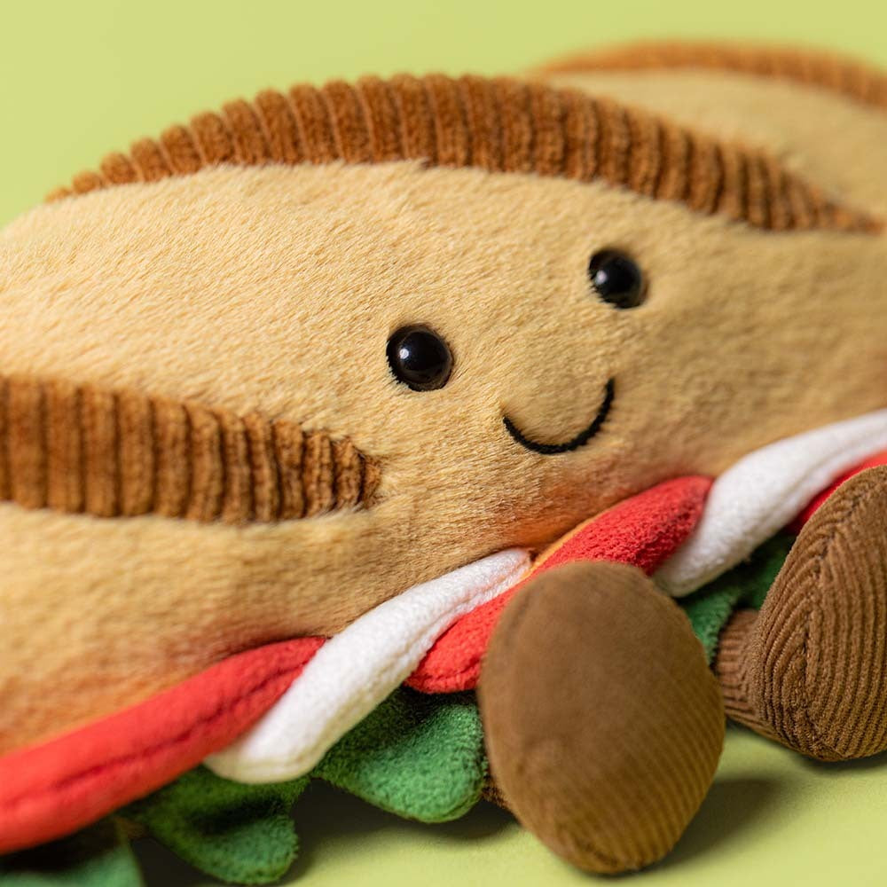 Plush toy resembling a hot dog with a smiling face on a green background