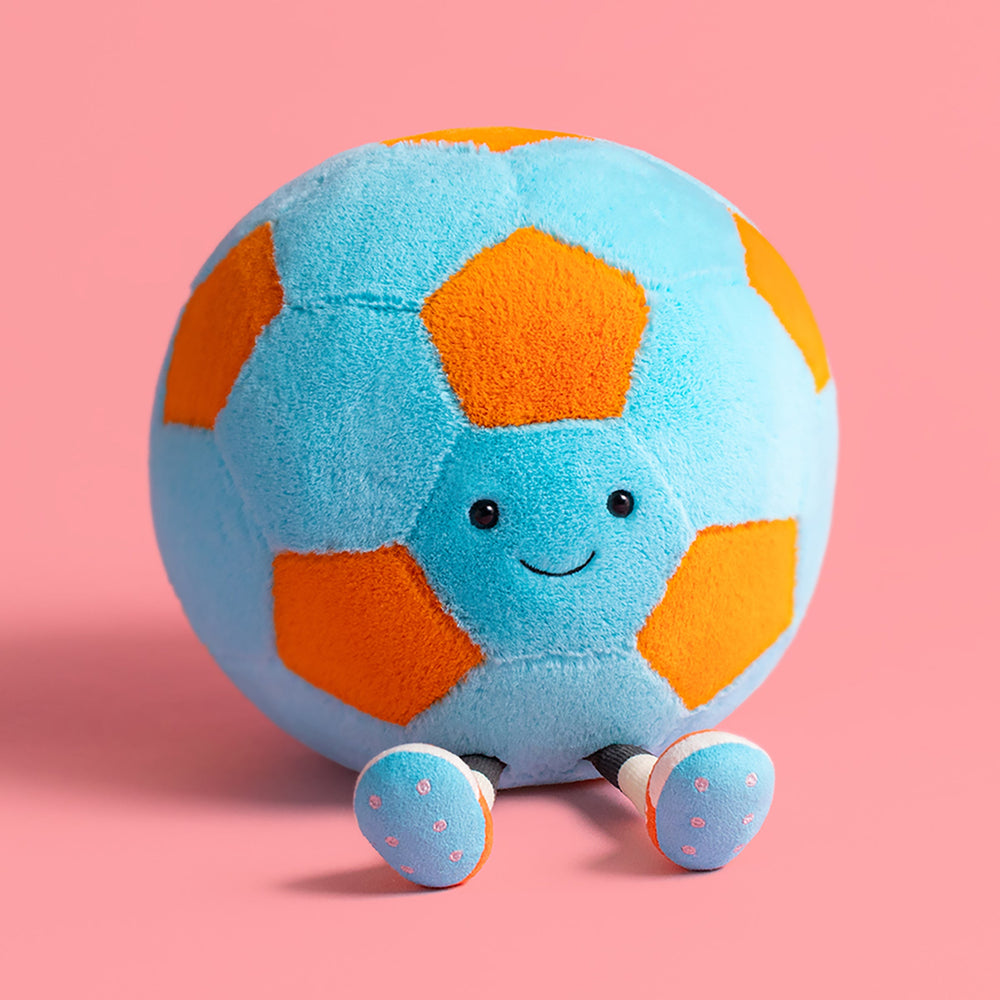 Plush toy soccer ball with a smiling face on a pink background