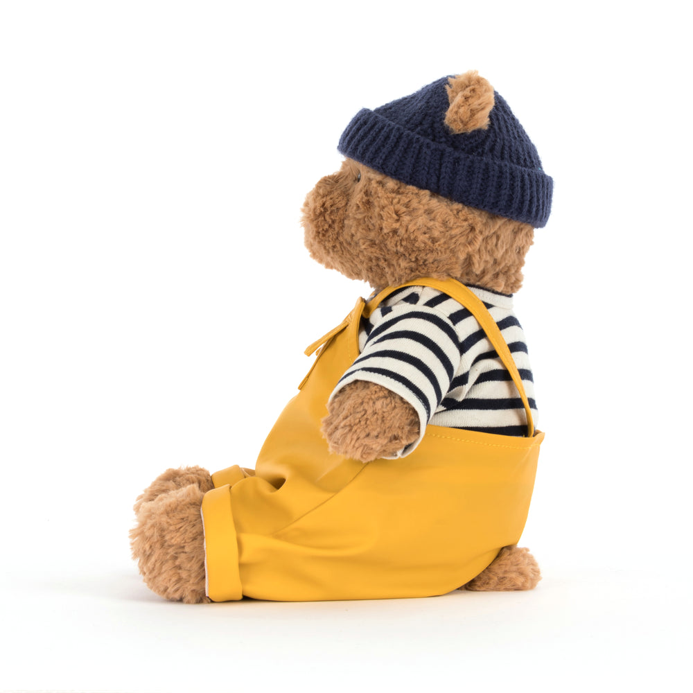 Teddy bear wearing a yellow raincoat, striped shirt, and navy hat on a white background