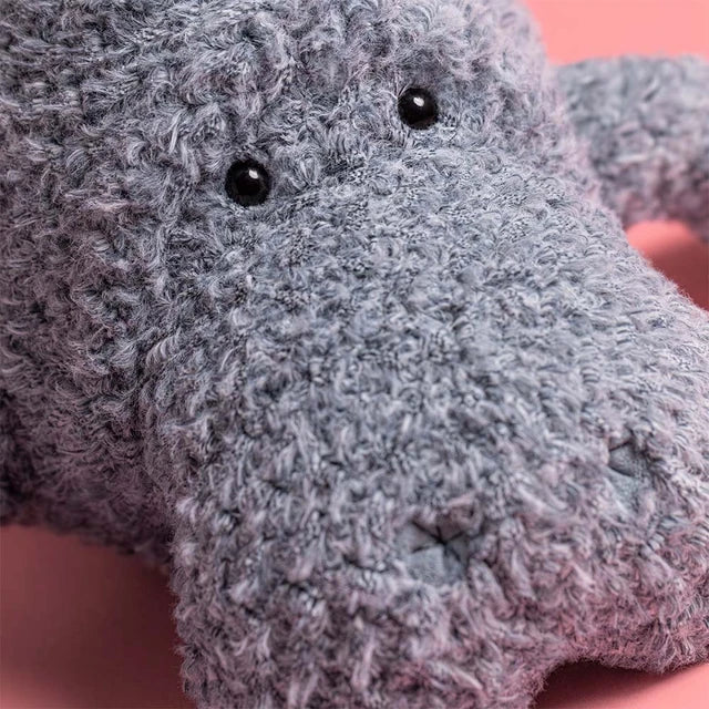 Close-up of a gray plush toy with black eyes on a pink background