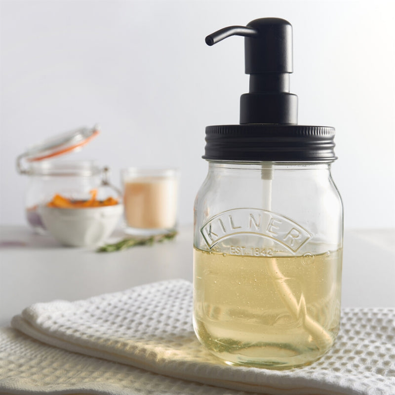 Glass jar with a black pump lid on a white surface, with a blurred background.