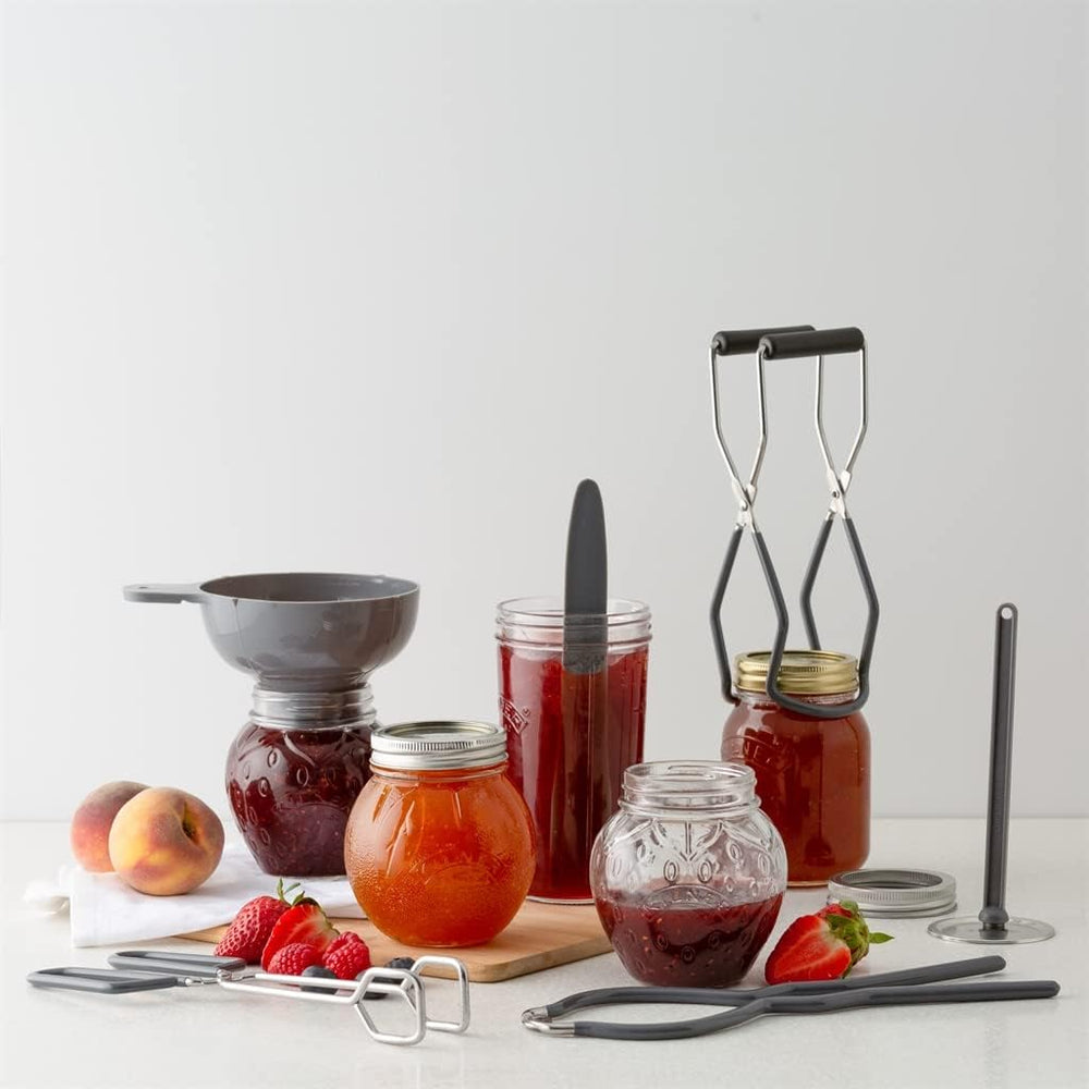 Jars of jam, a funnel, a ladle, and other canning tools on a white surface with a light gray background.