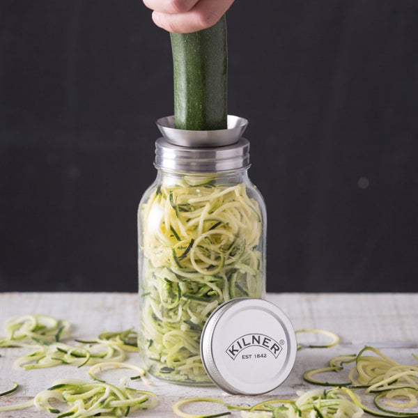 Kilner jar with zucchini noodles being made using a spiralizer on a wooden surface.