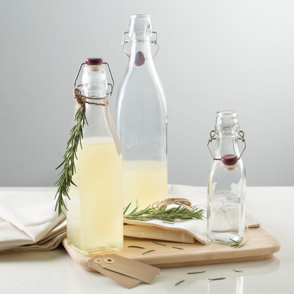 Three glass bottles with herbs on a wooden board against a light gray background