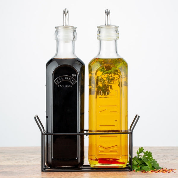 Two glass bottles, one black and one yellow, in a metal stand on a wooden surface with a white background.