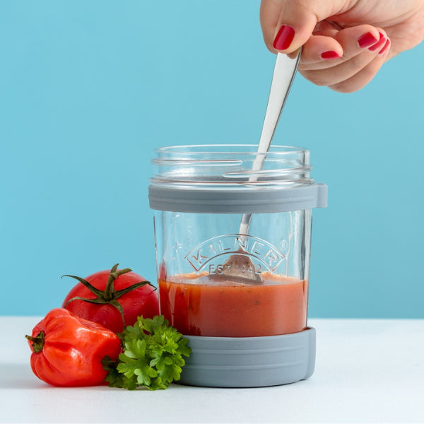 Glass jar with red liquid, spoon, and vegetables on a blue background