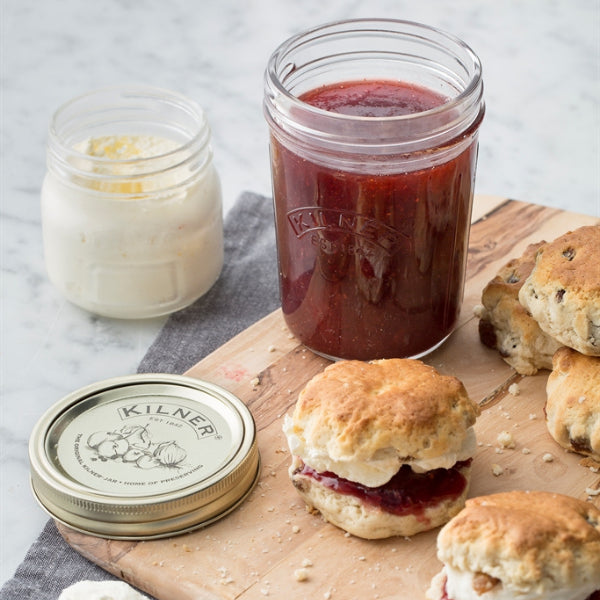 Kilner jars with jam and cream on a wooden board with scones.