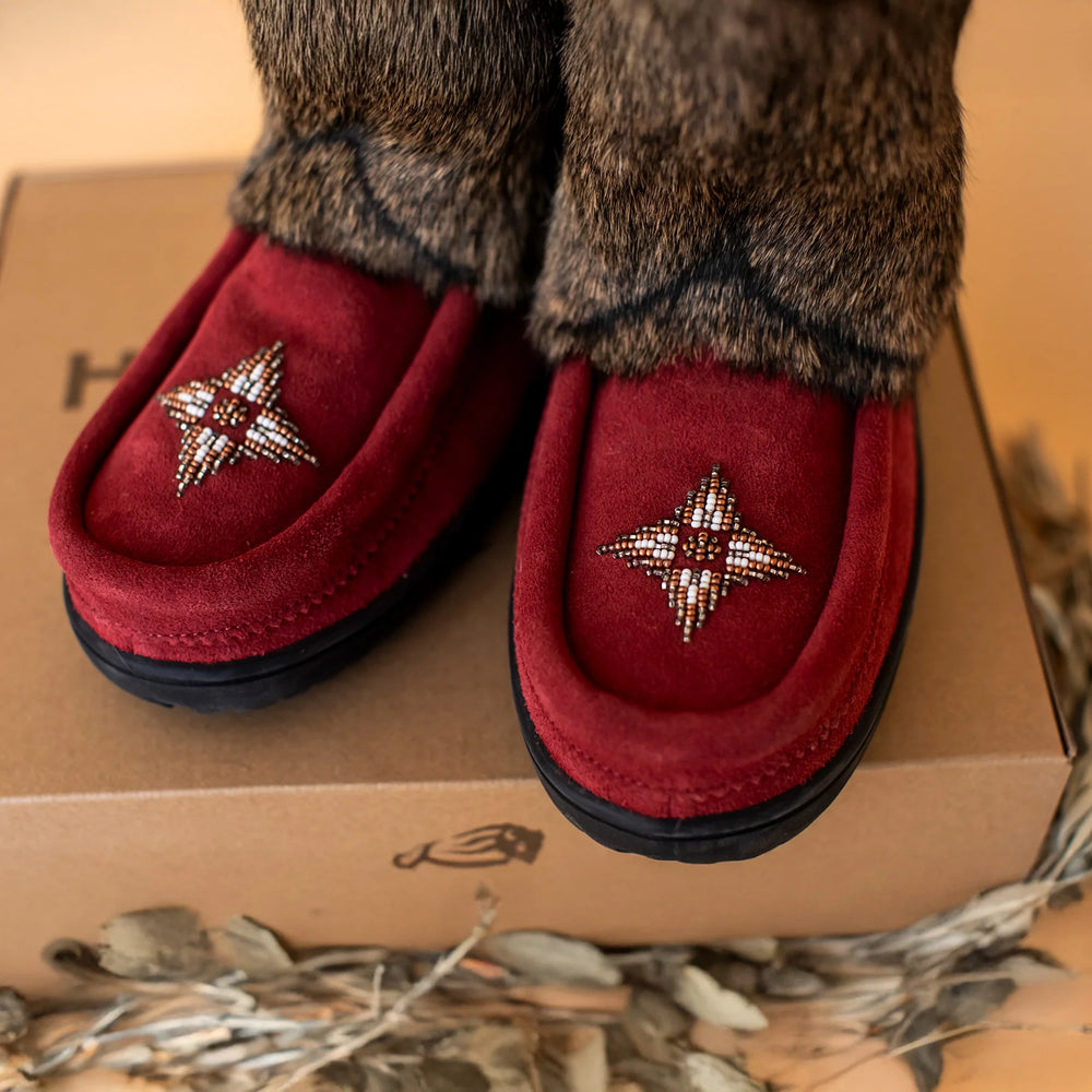 Red mukluk with geometric beadwork sit on a cardboard box. 