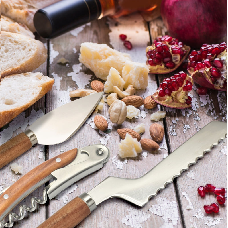 Wooden and metal cheese tools with sliced bread, cheese, nuts, and pomegranate seeds on a wooden surface.