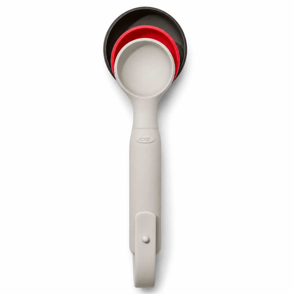 A set of three nested measuring cups in black, red, and white, stacked vertically on a clean white background. The handle has a small embossed 'OXO' logo near the top.