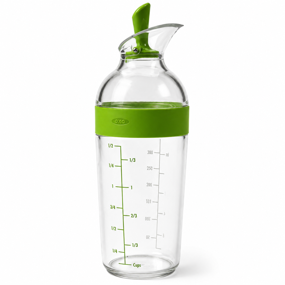 A clear glass oil dispenser bottle with a bright green lid and a green measurement band showing liquid levels in cups and milliliters.